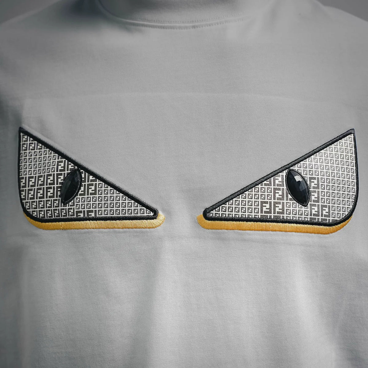 Close-up of Fendi white T-shirt chest: black and gray patterned eye applique with gold trim