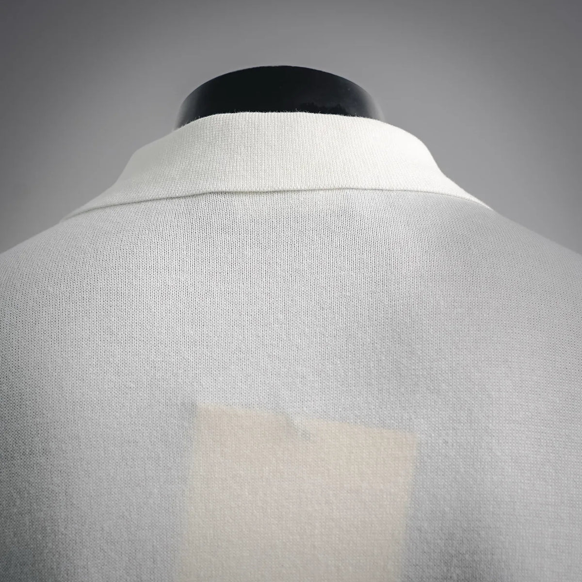 White polo shirt back with raised collar seam and smooth knit texture.