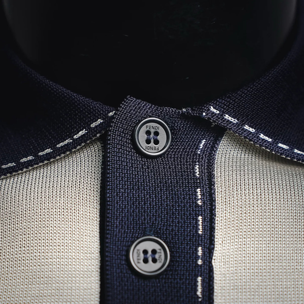 Fendi polo placket close-up with navy fabric panel, topstitching, and logo button