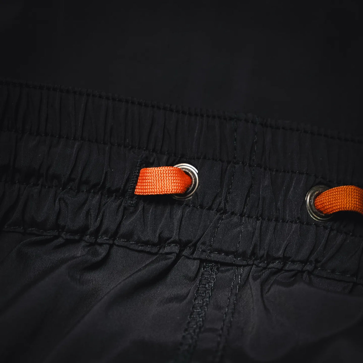 Black shorts waist with orange drawstring cords and metal eyelets
