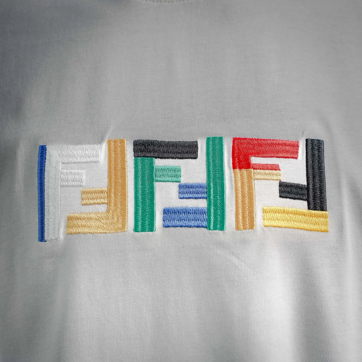 White T-shirt chest embroidery close-up with multicolor geometric logo stitches