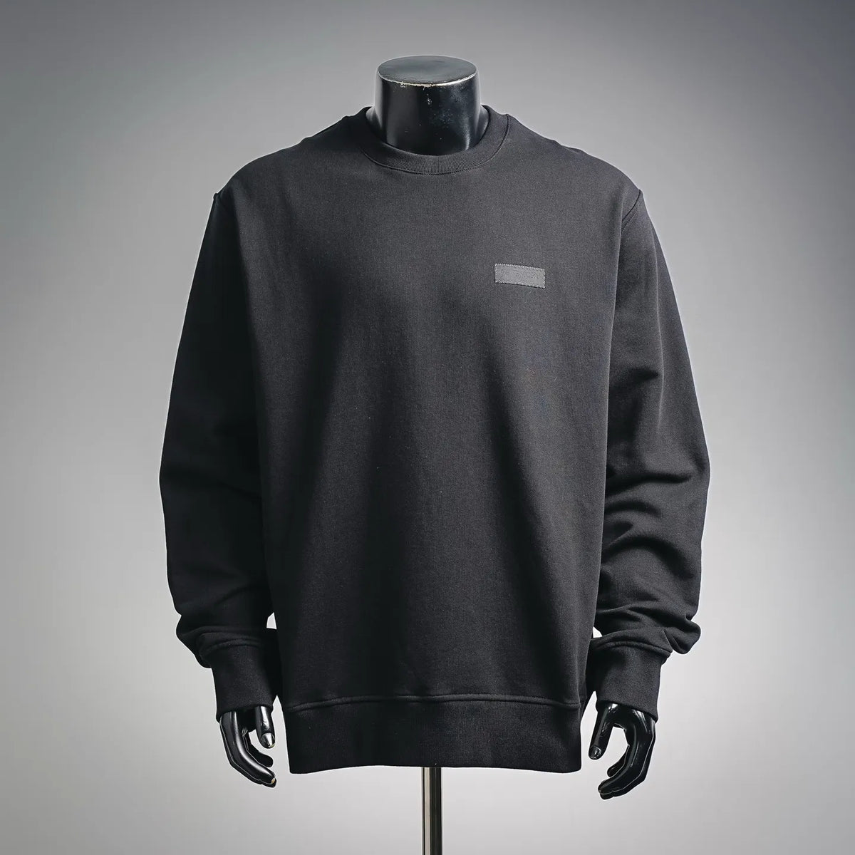Black crewneck sweatshirt with ribbed collar and small chest logo patch