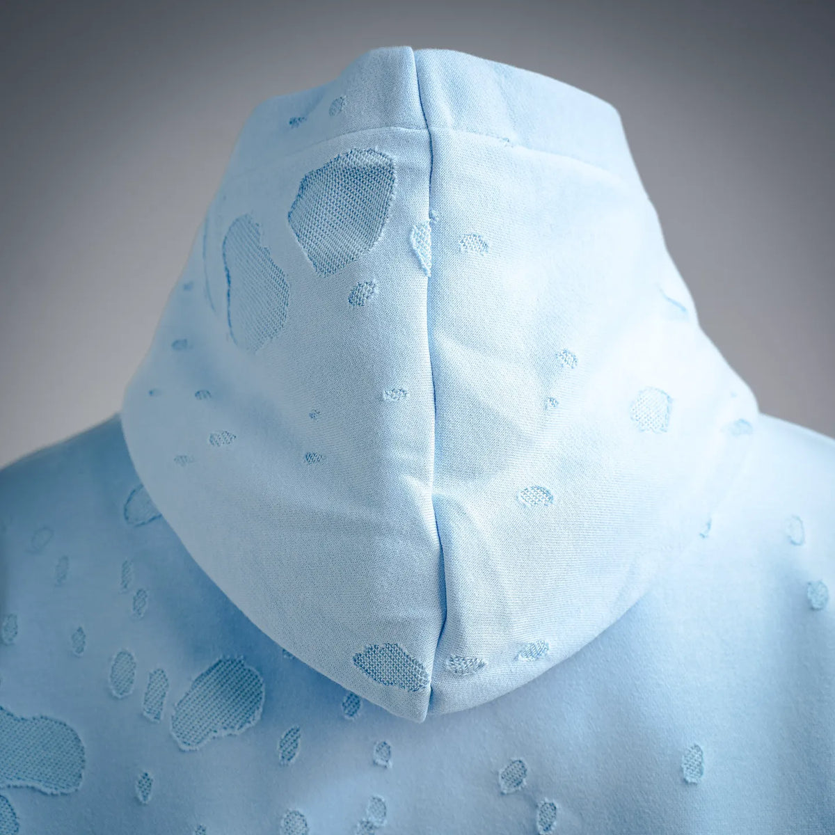 Light blue hoodie close-up with textured fabric and draped hood detail