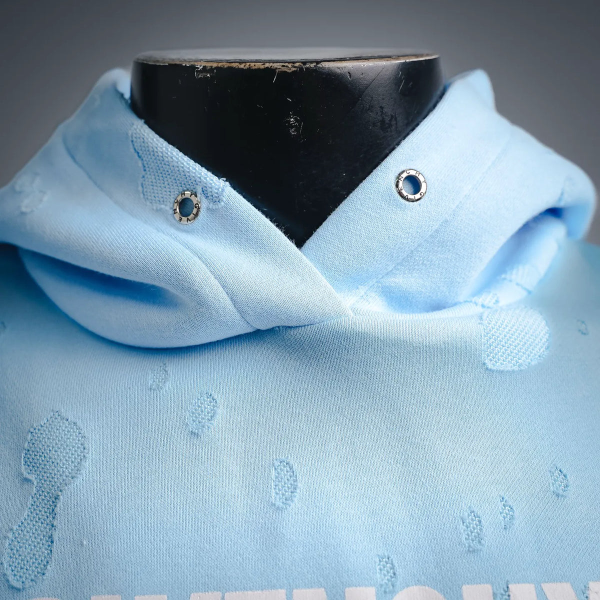 Light blue hoodie collar close-up with metal eyelets and fabric drawstrings