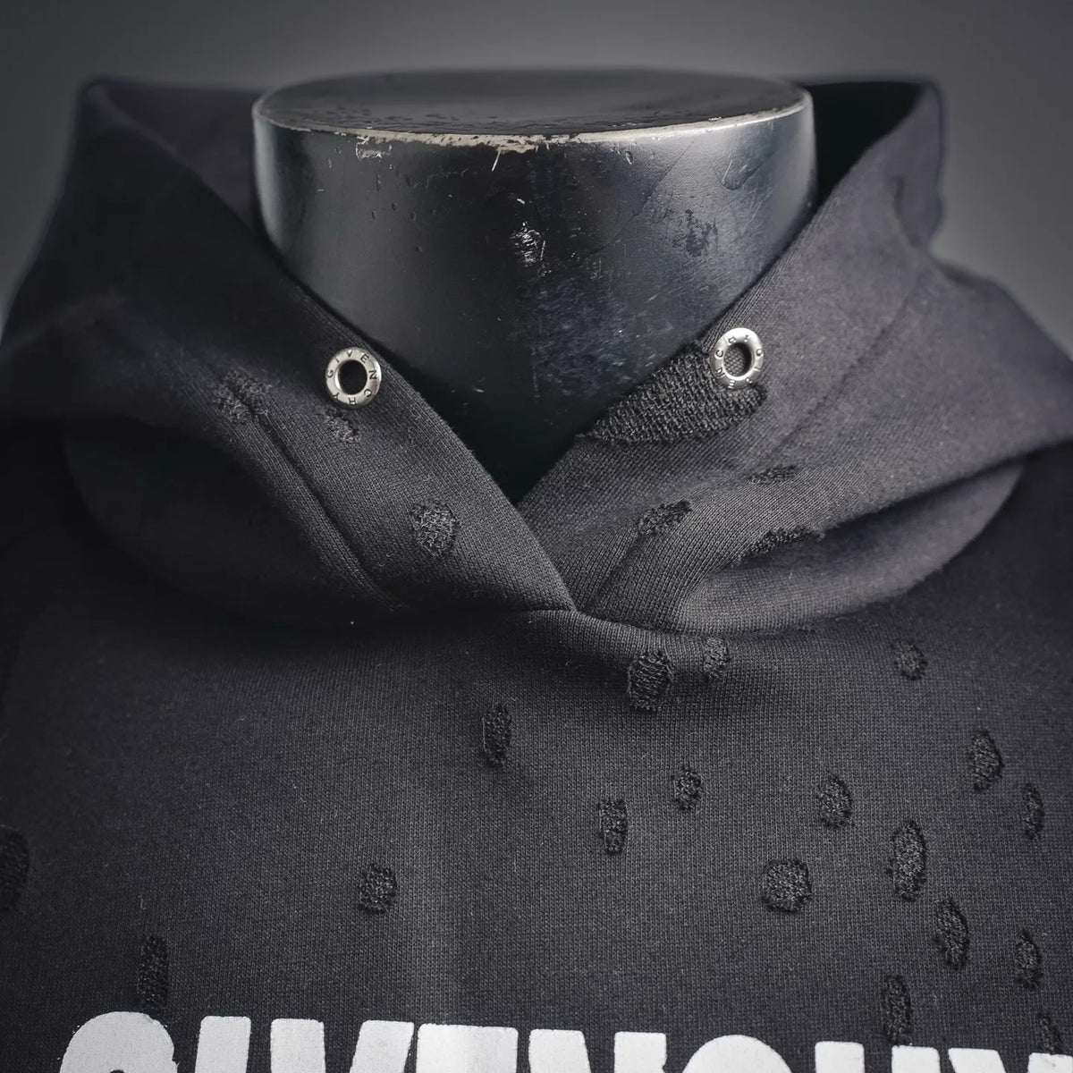 Front collar of black hooded sweatshirt with eyelet details and logo textured fabric
