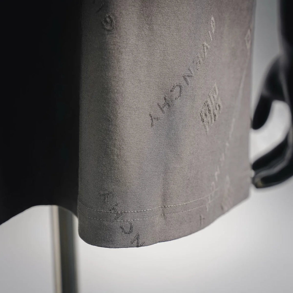 Gray short-sleeve T-shirt hem detail with subtle stitched pattern and logo print.