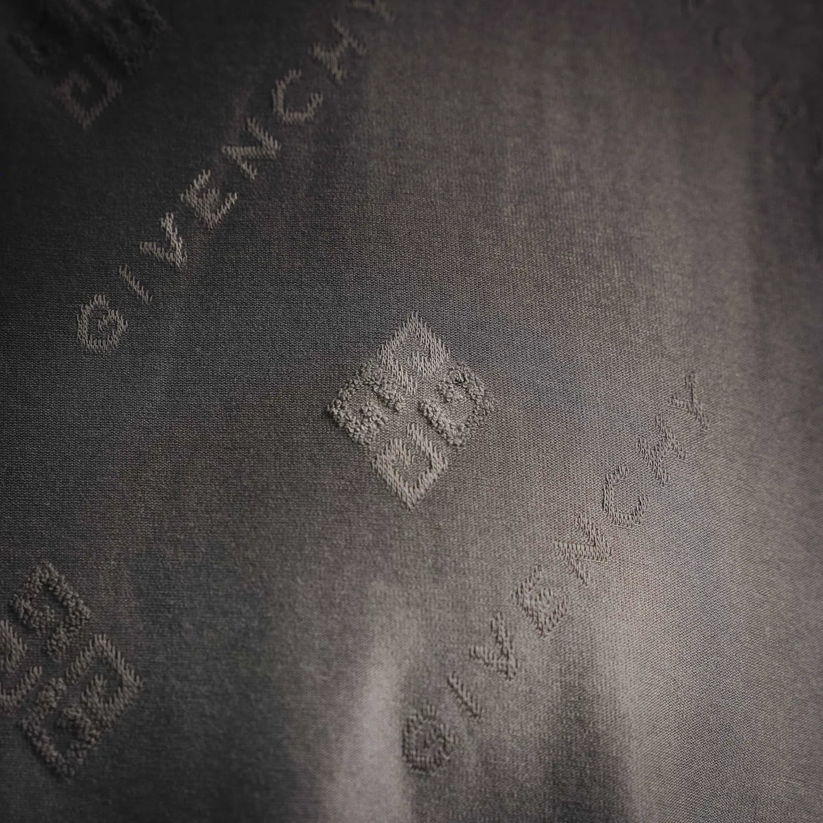 Gray short-sleeve T-shirt close-up of textured fabric with small repeating logo icons.