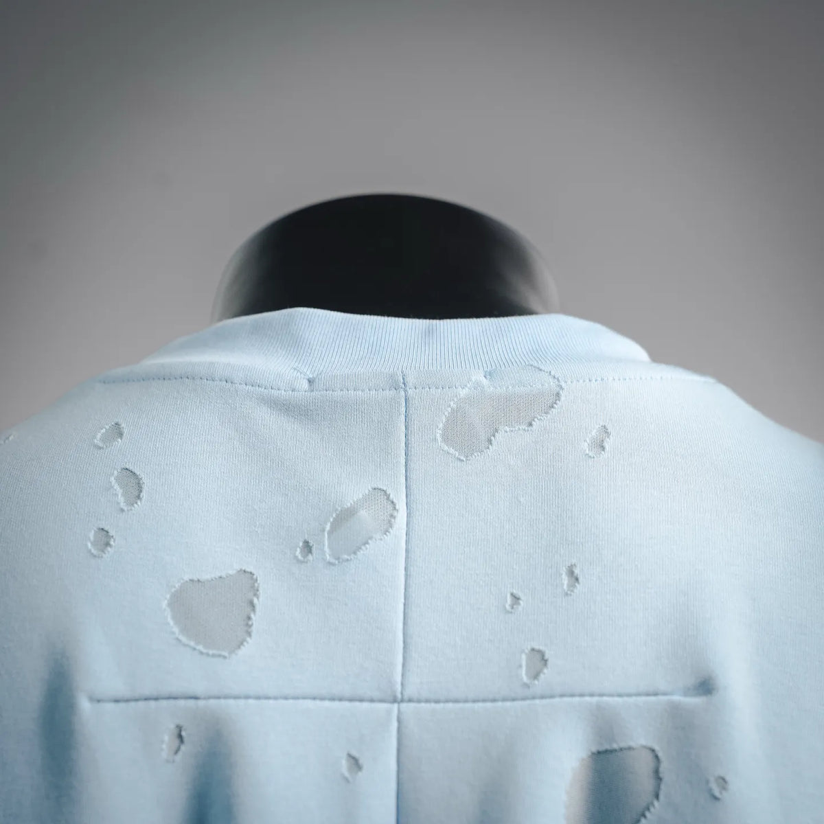 Light blue T-shirt back with central seam and scattered raised logo marks