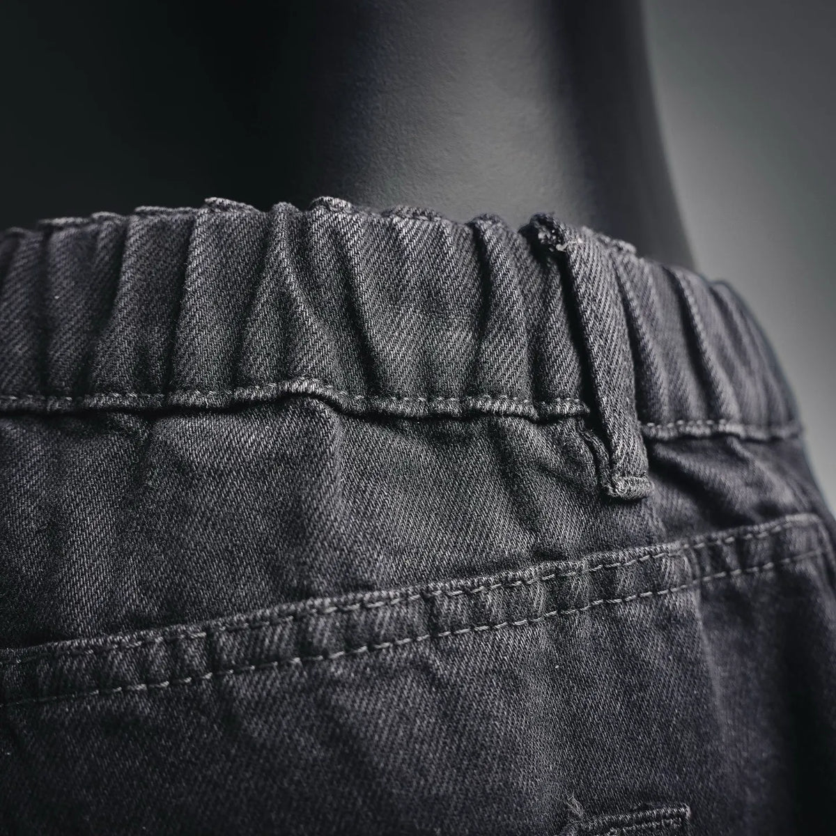 Elastic waistband and stitched waistband seam on black denim pants.