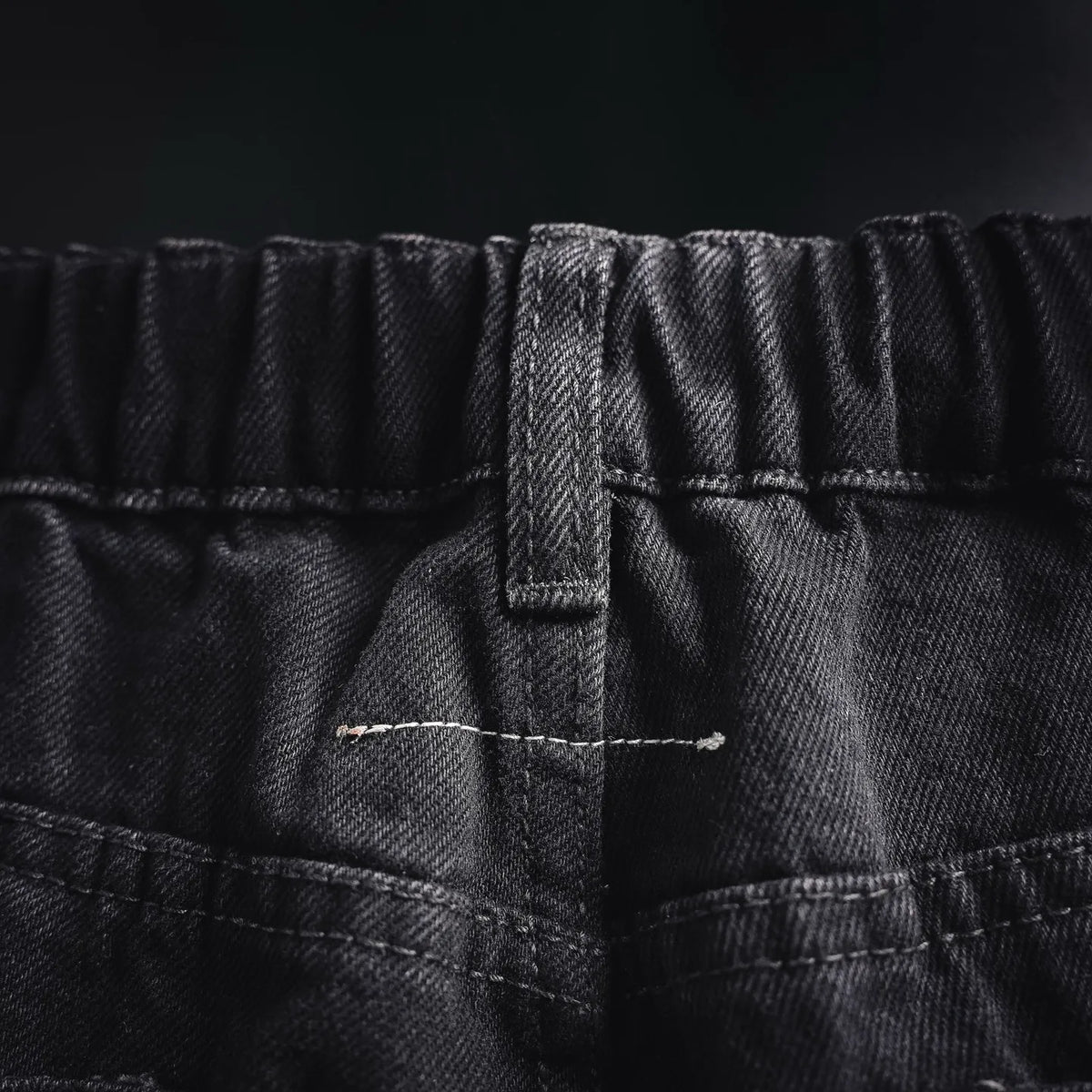 Front fly and waistband stitching on black denim pants with button closure.