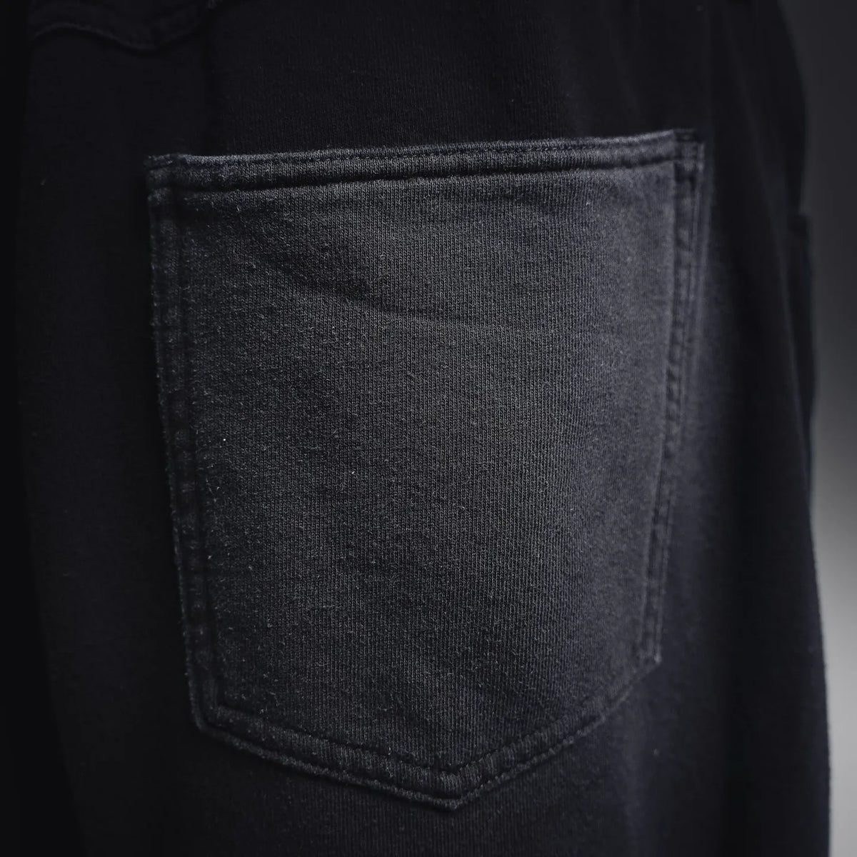 Close-up of black denim fabric and front pocket with stitched edge