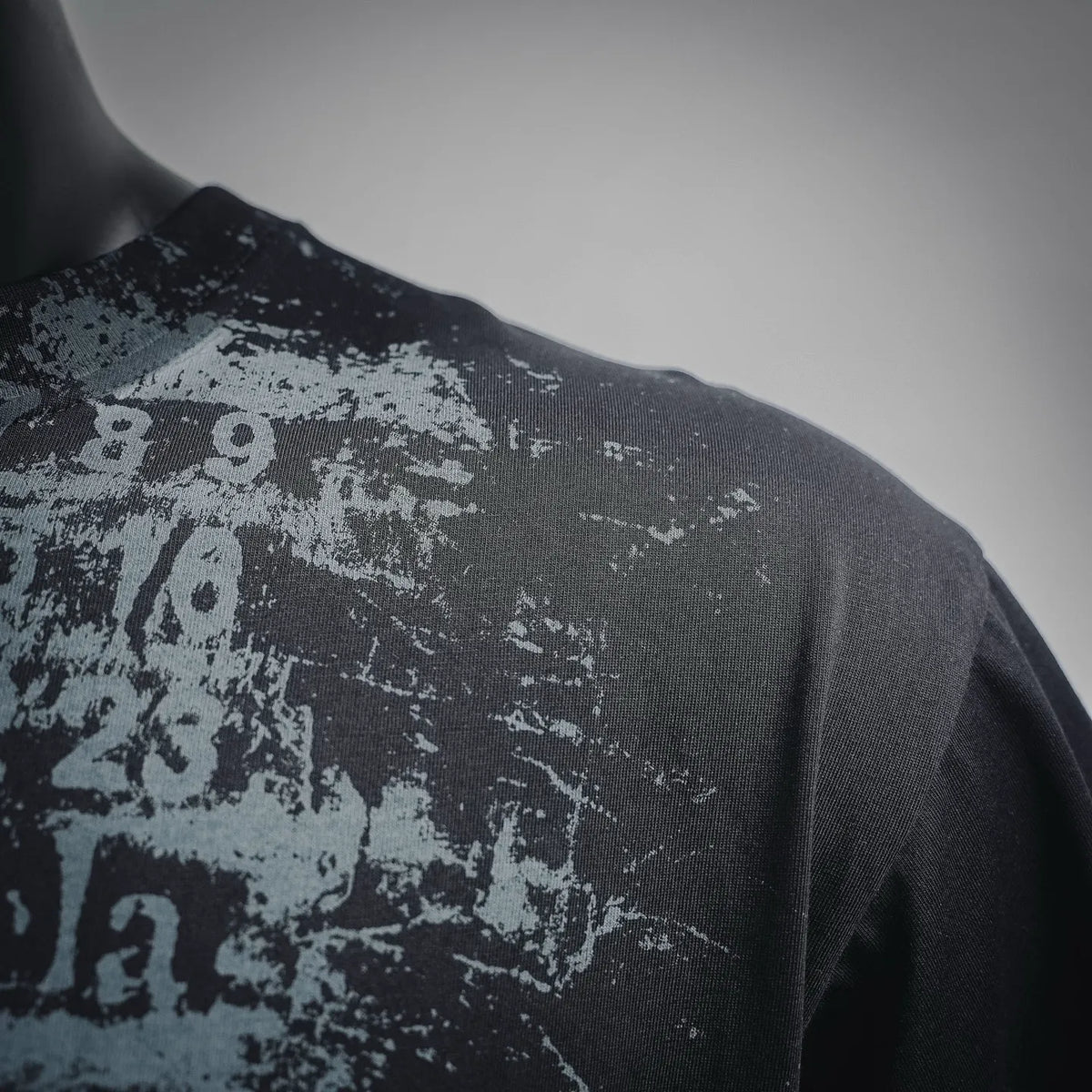 Black T-shirt shoulder close-up with distressed grey printed numbers