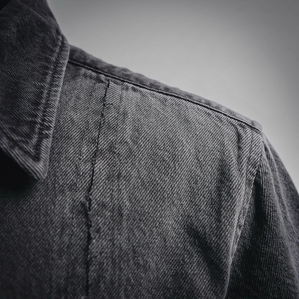 Black denim shirt shoulder close-up with yoke seam and folded collar