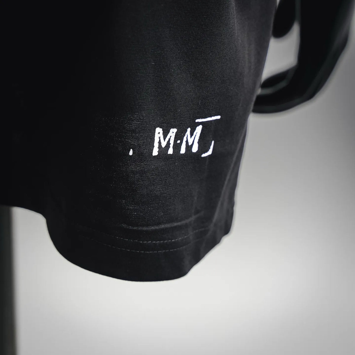 Black T-shirt hem with small white MM logo print