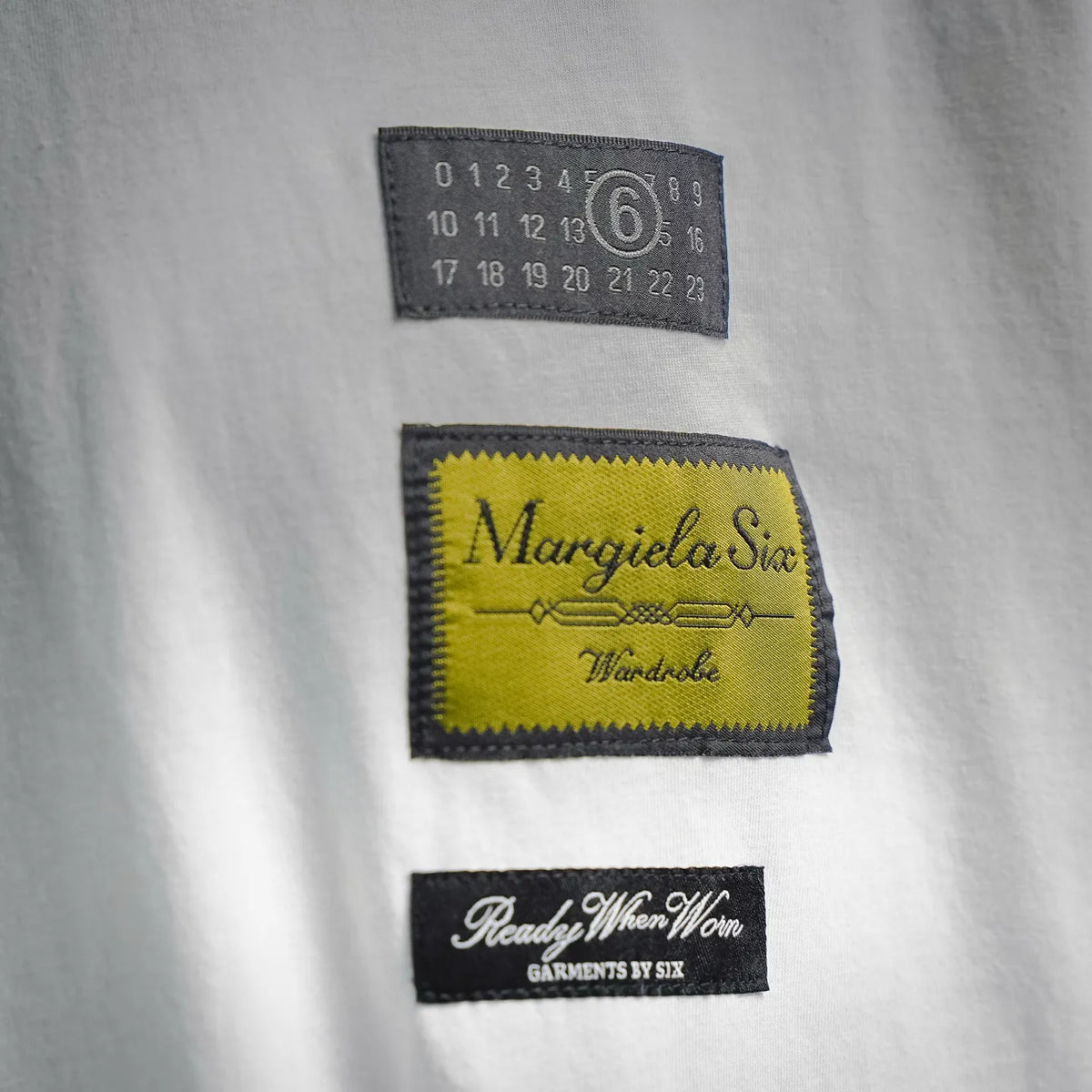 T-shirt chest labels: black numbers tag, yellow logo patch, and black text patch