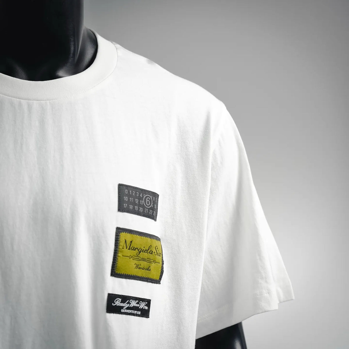 White T-shirt sleeve area with three small rectangular logo patches on chest