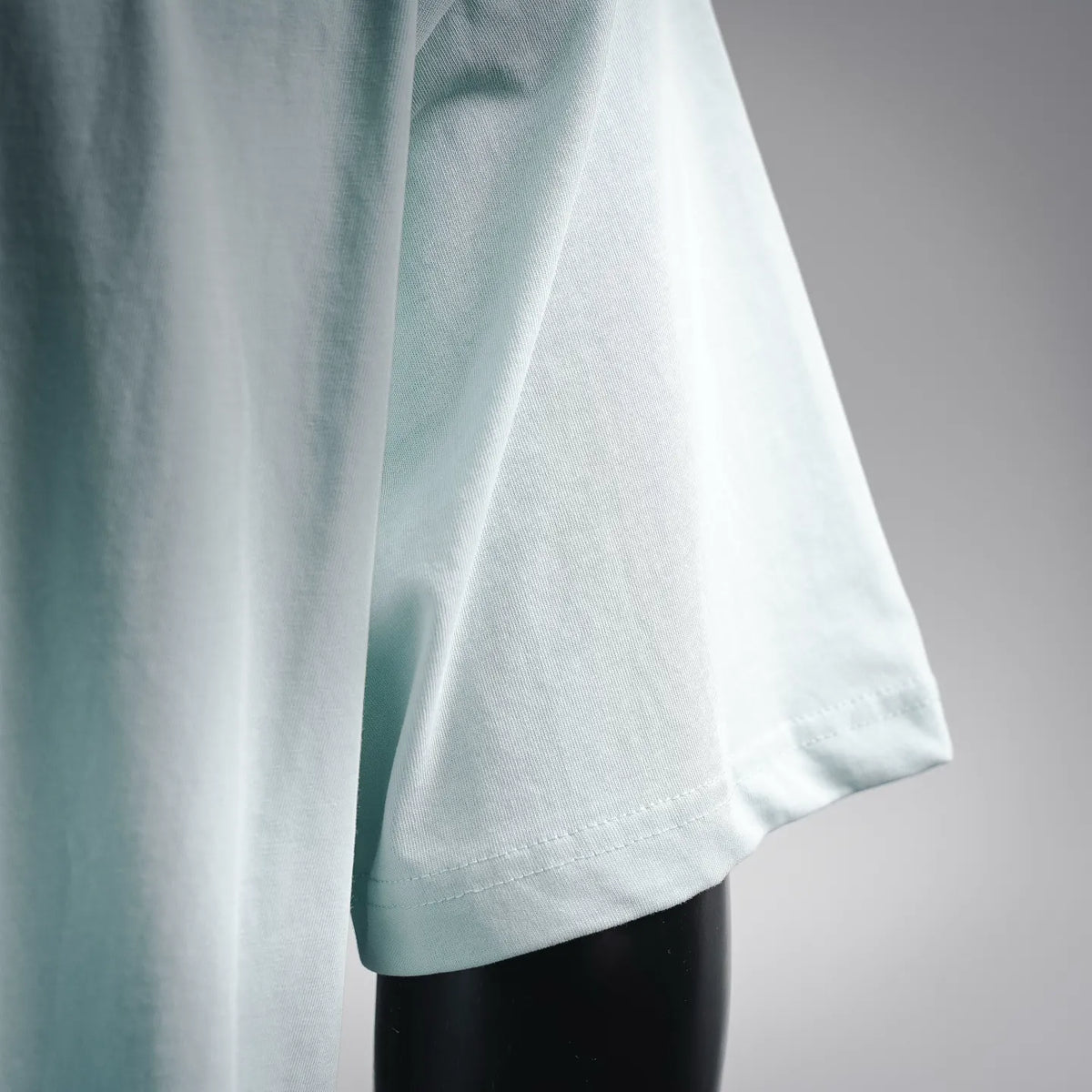 Light blue T-shirt side with stitched hem and faint number print