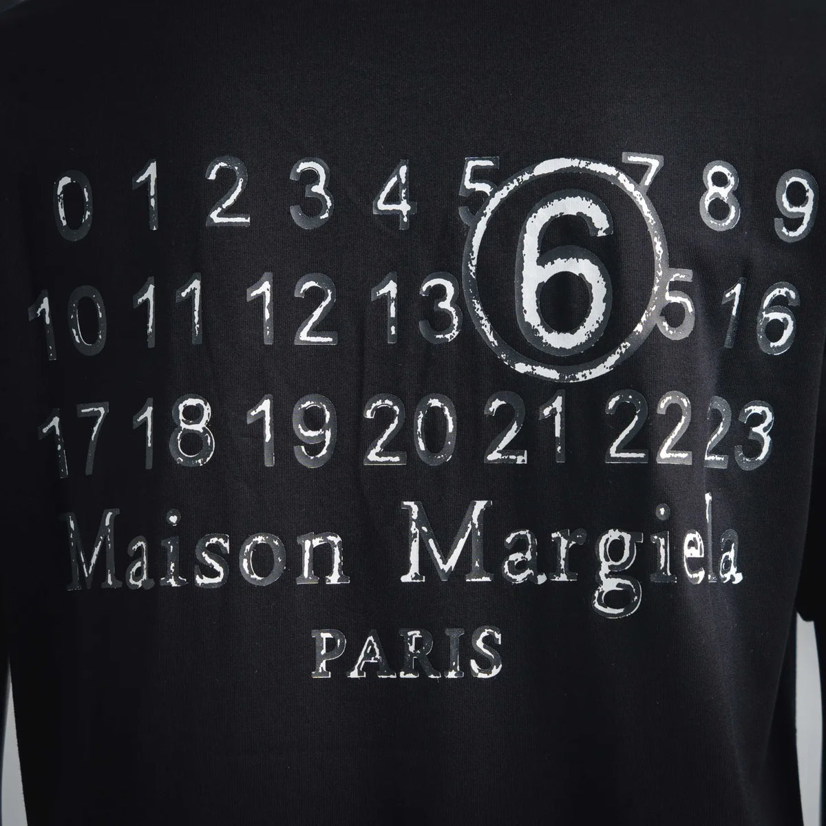 Close-up of '6' numeric print and 'Maison Margiela' lettering on black t-shirt