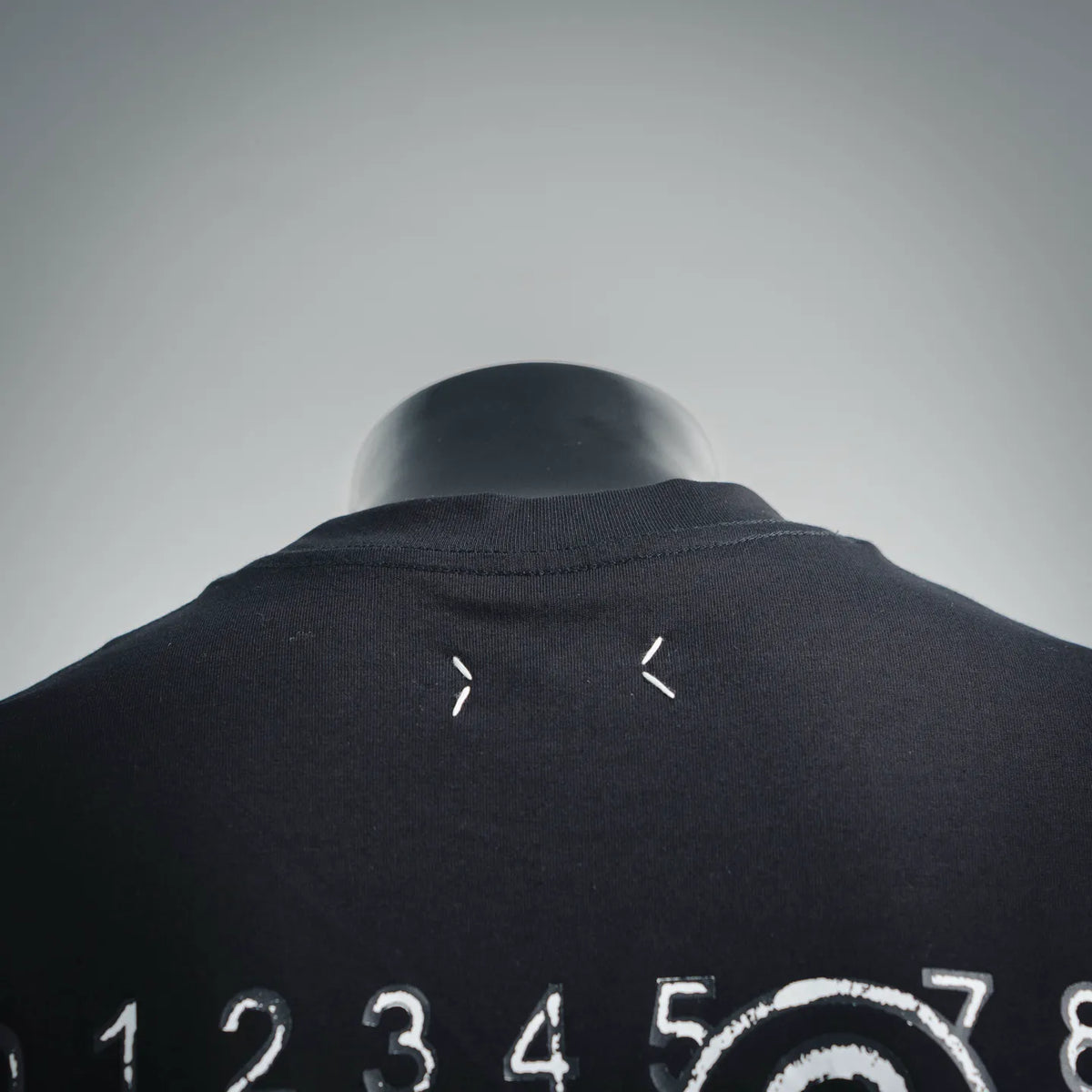 Back of black short-sleeve t-shirt with small white arrow-like marks near collar