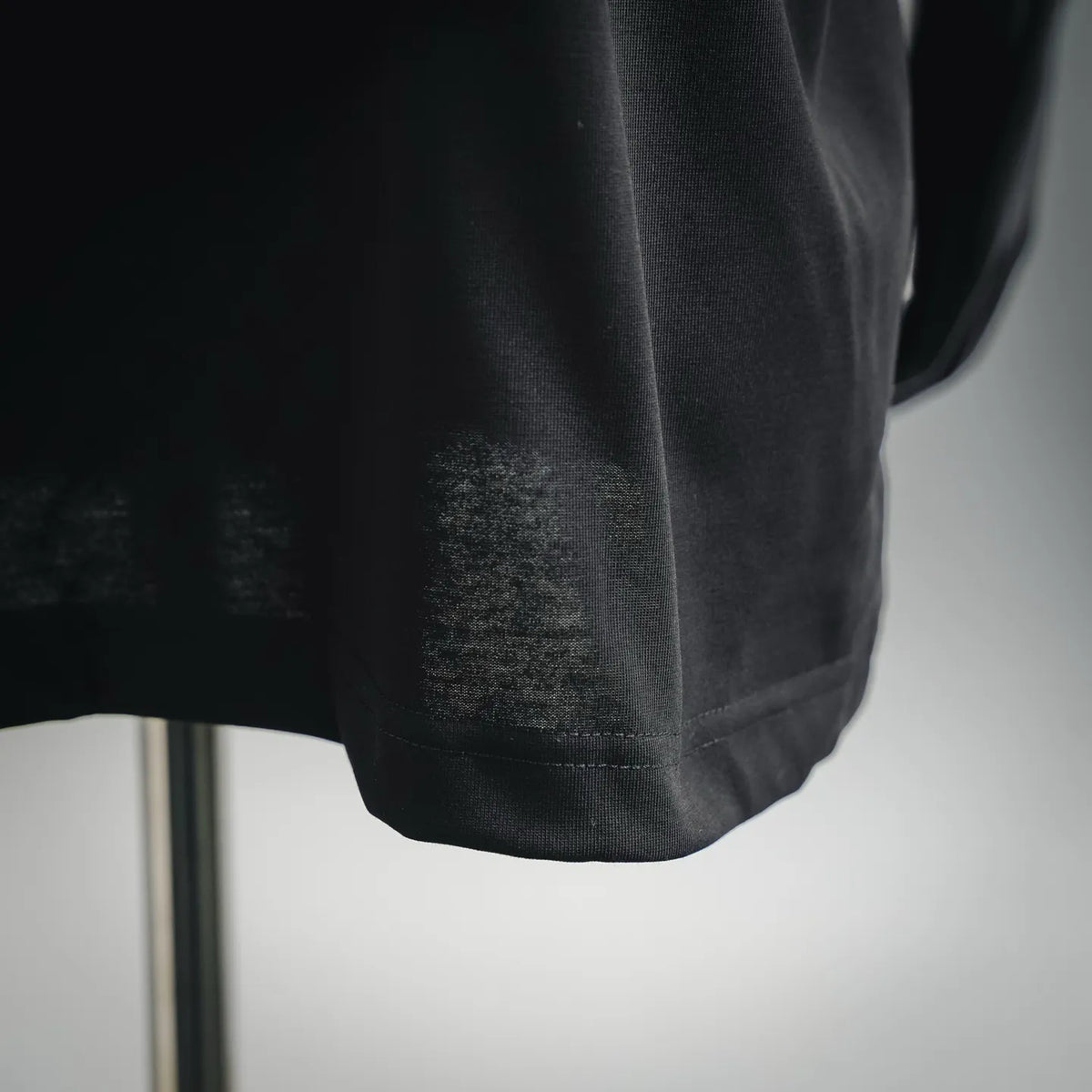 Black short-sleeve T-shirt hem close-up with visible stitching and slight wear.