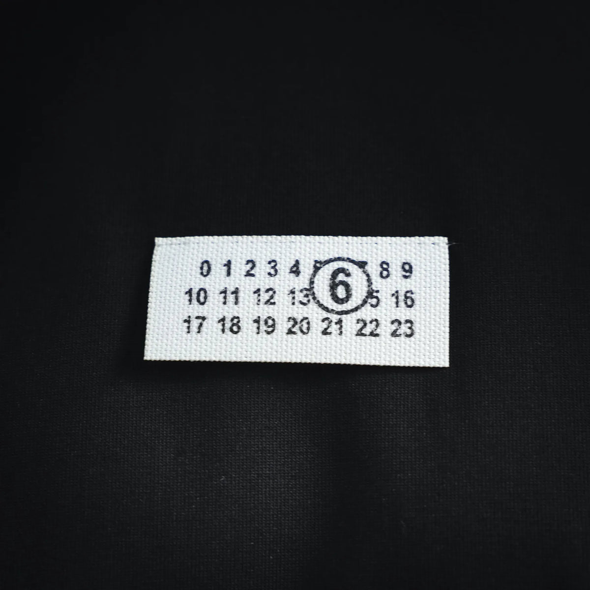 Black T-shirt size label patch with white background and black numerals.