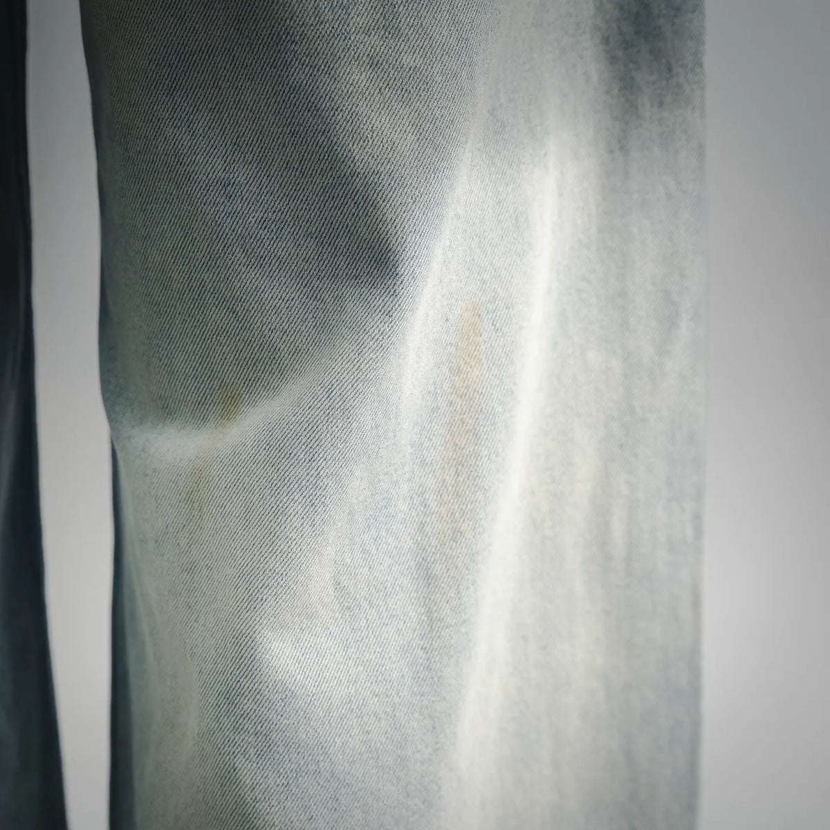 Light-wash denim fabric close-up with visible weave and subtle distressed speckling
