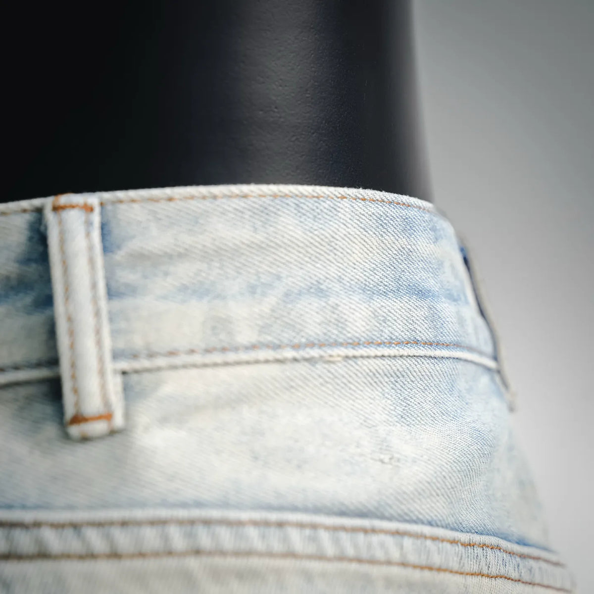Light-wash denim waistband detail with belt loop and orange topstitching