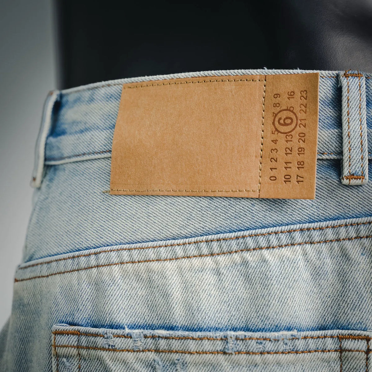 Light-wash denim pants with tan size label and orange seam stitching near pocket