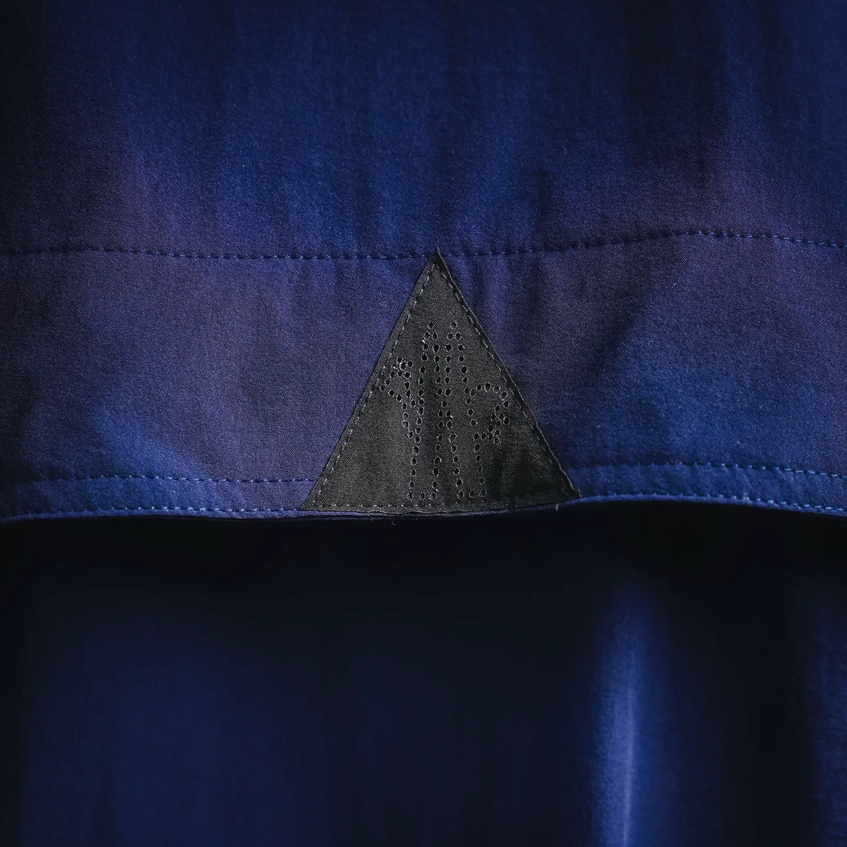 Blue jacket fabric close-up with perforated black triangular insert