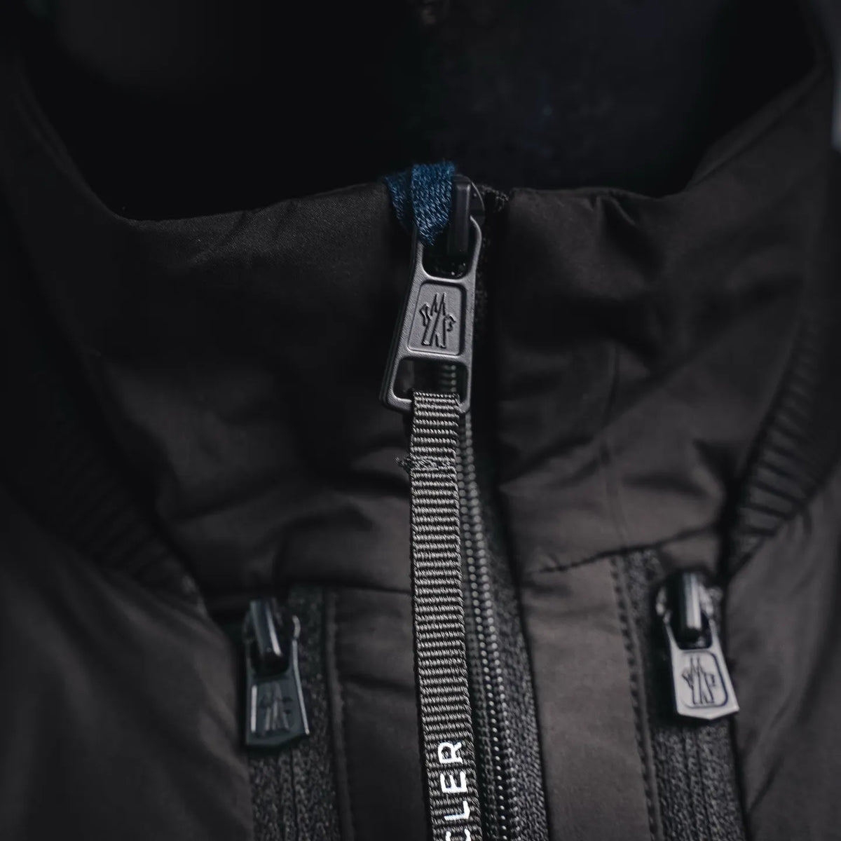 Moncler coat zipper close-up with two metal pulls and branded tab