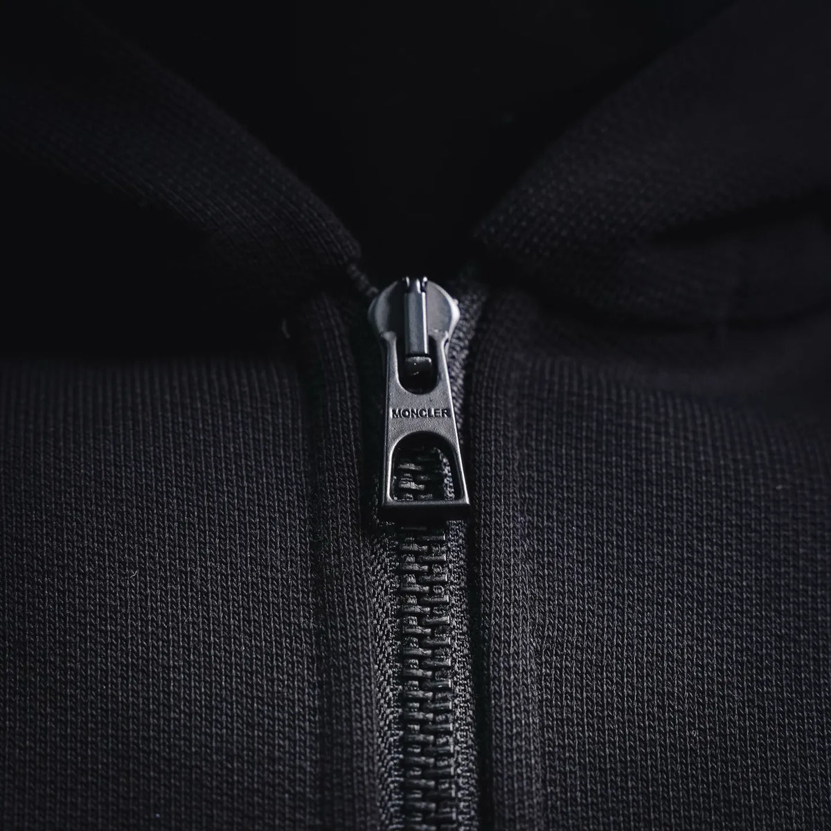 Close-up of zip pull with Moncler branding on black hoodie.