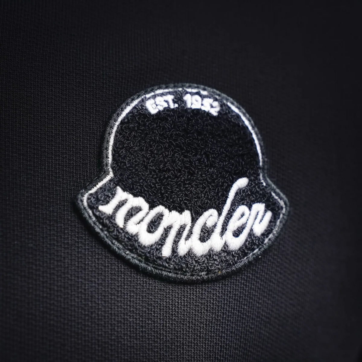 Embroidered Moncler logo patch on black hoodie chest.