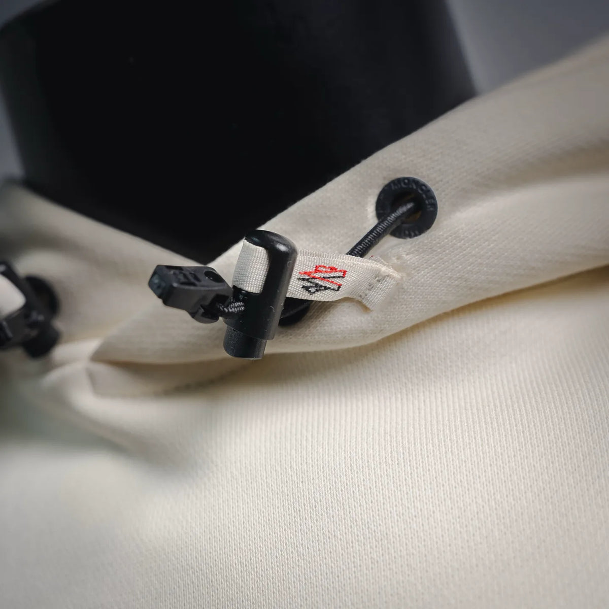 Cream hoodie neck hardware with black adjuster and small logo patch
