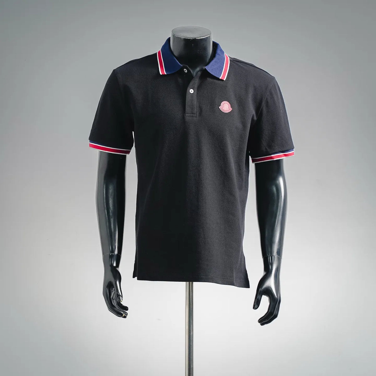Black short-sleeve polo shirt with blue-red striped collar and pink logo patch