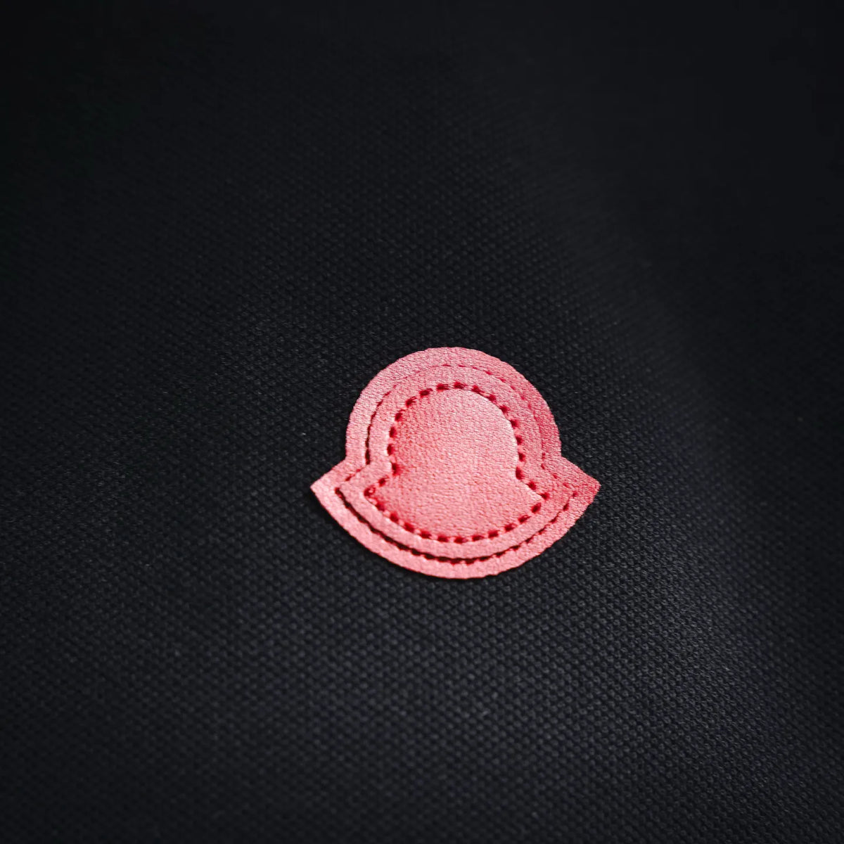Pink circular logo patch on black polo shirt chest