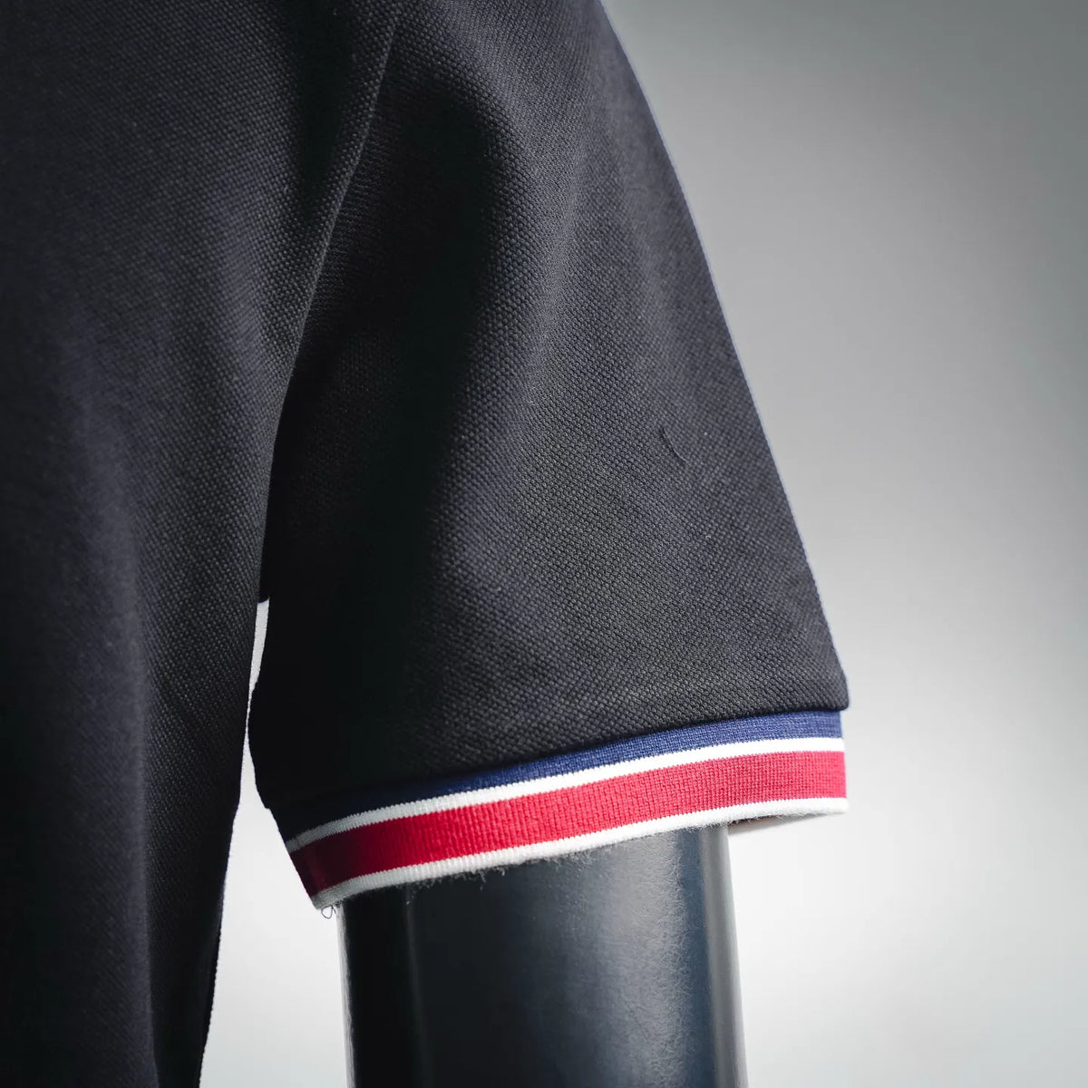 Black polo shirt sleeve with blue, white, and red striped cuff trim