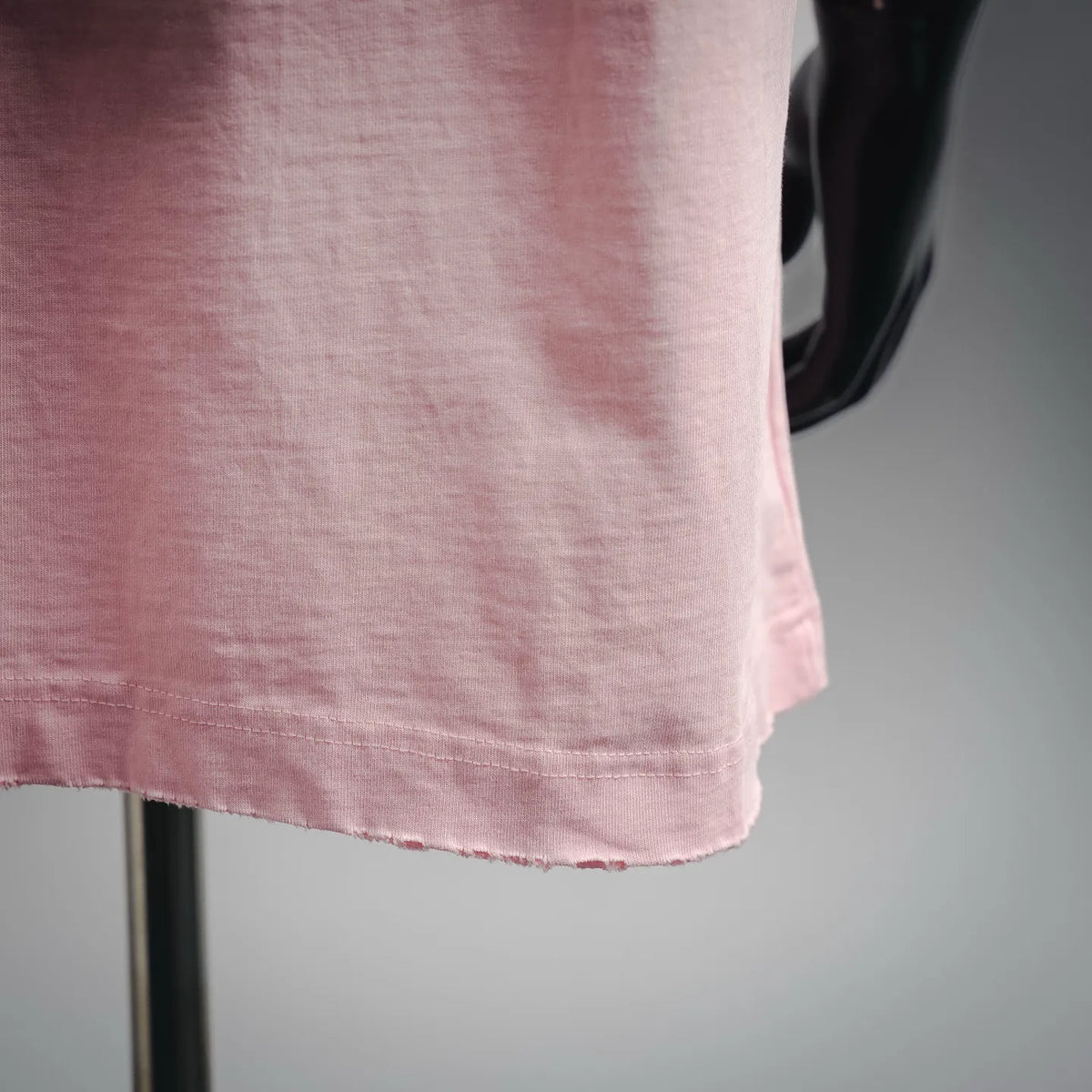 Pink crew-neck T-shirt hem with visible stitching and slight fabric texture