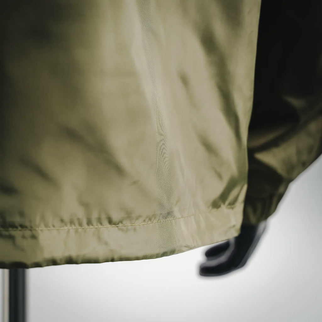 Olive green jacket hem with stitched edge and gathered bottom, shown in close-up