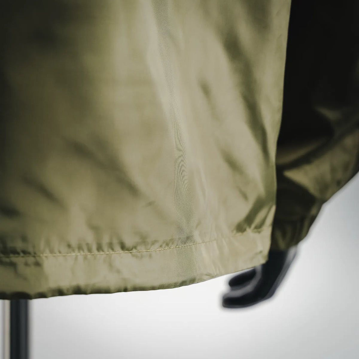 Olive green jacket hem with stitched edge and gathered bottom, shown in close-up