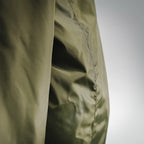 Side panel of an olive green jacket with vertical seam stitching, close-up view