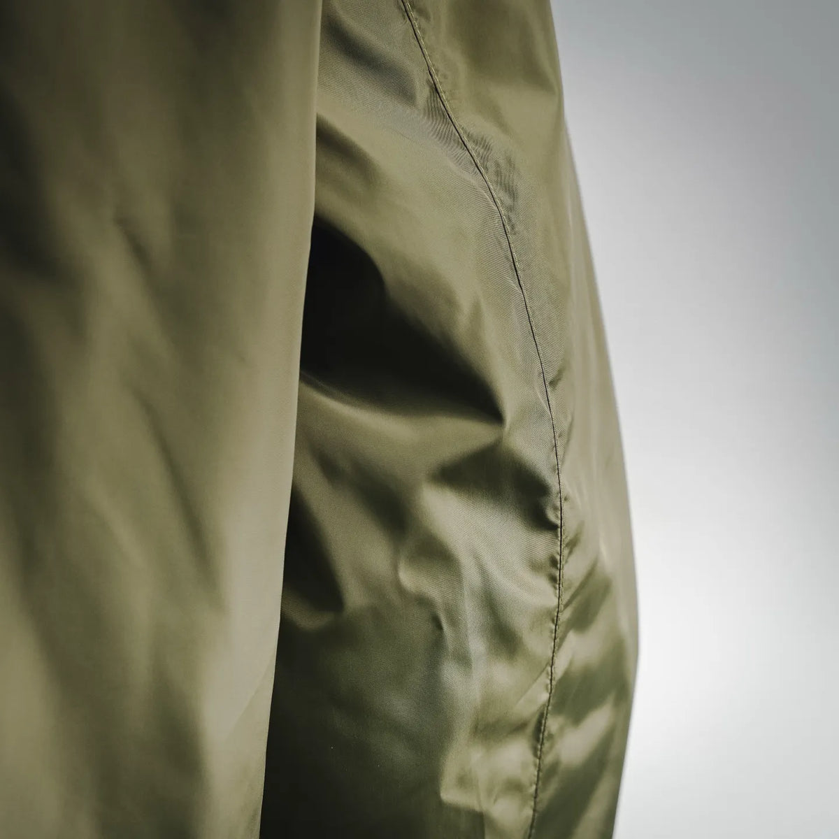Side panel of an olive green jacket with vertical seam stitching, close-up view