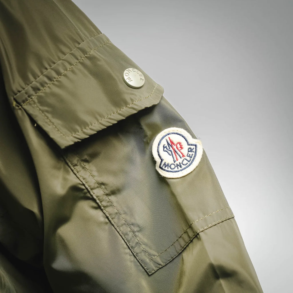 Olive green jacket sleeve with Moncler patch and small round logo badge, close-up