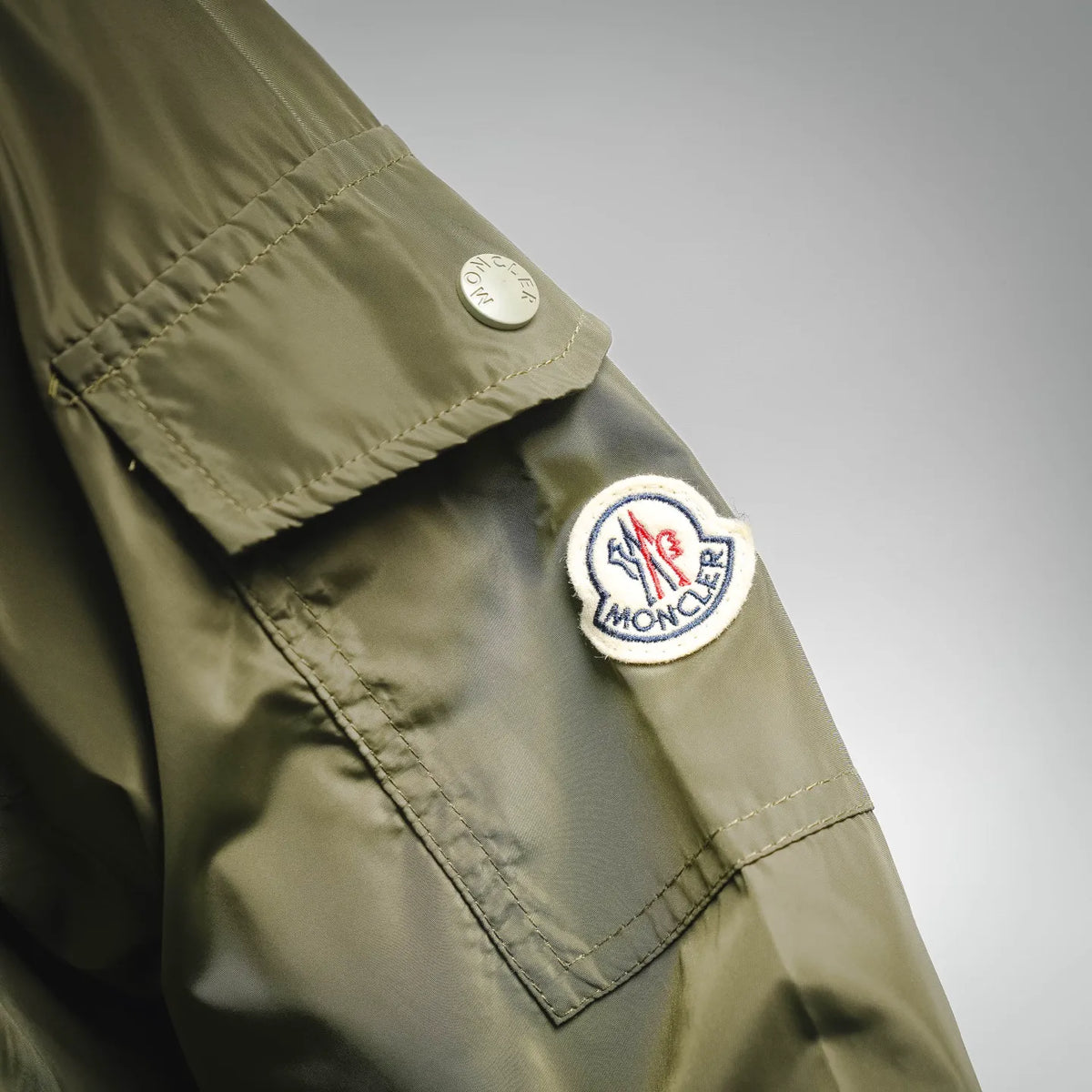 Olive green jacket sleeve with Moncler patch and small round logo badge, close-up
