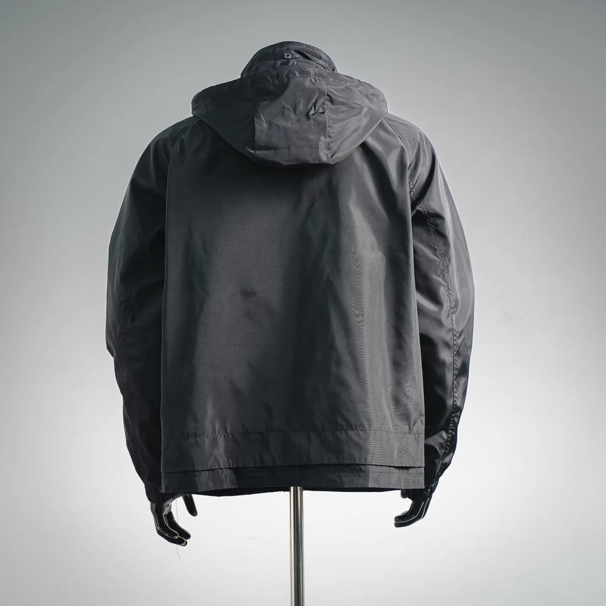 Dark hooded coat, back view, with adjustable hood and elastic hem.