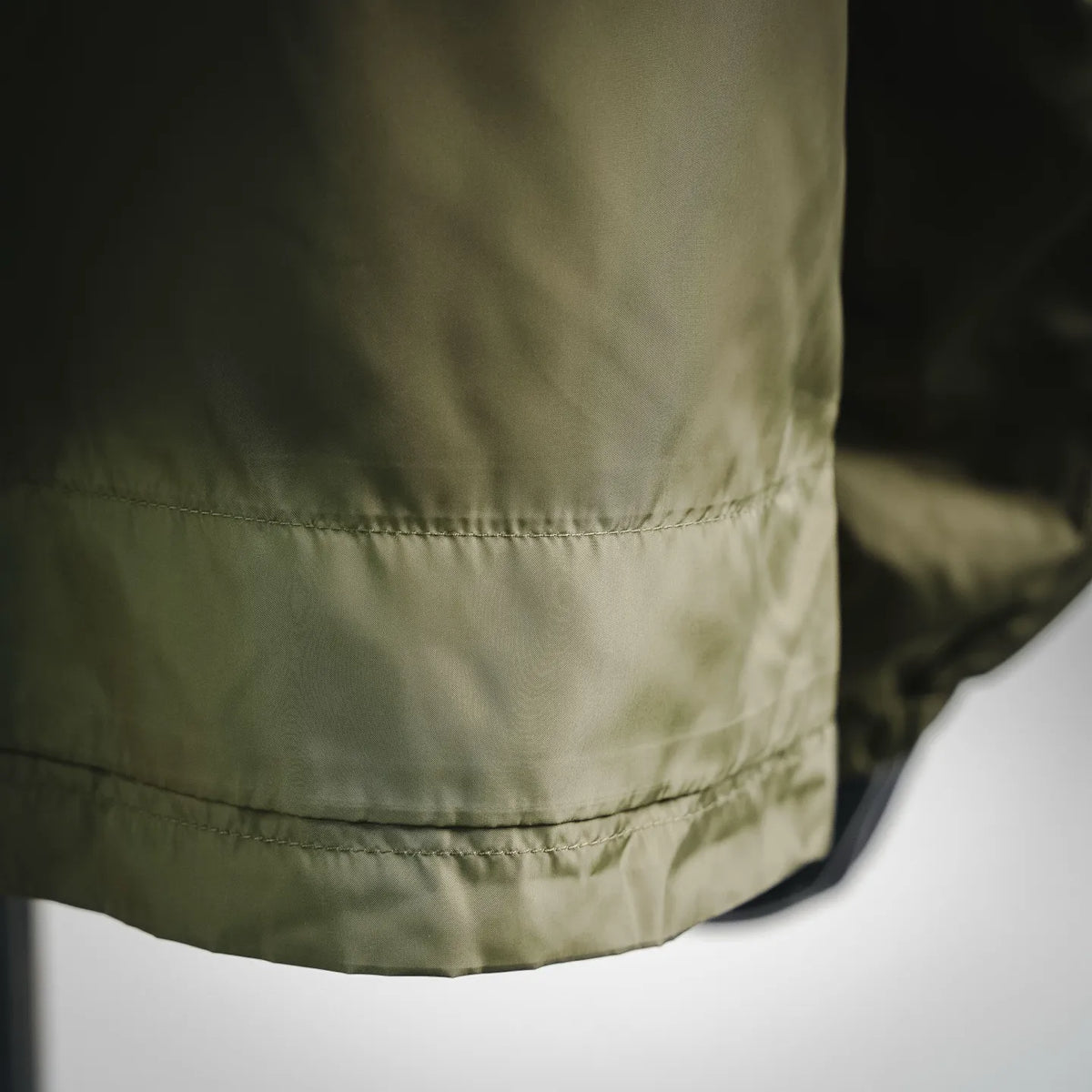 Olive coat hem with elastic finish and visible stitching close-up
