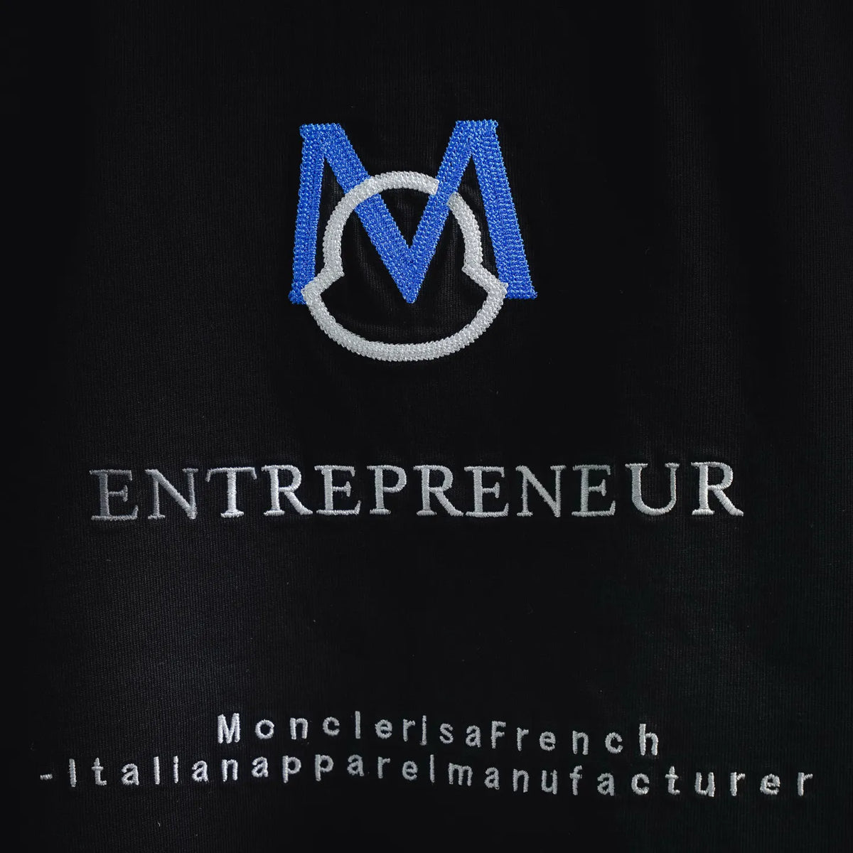 Black T-shirt chest graphic with blue Moncler M emblem and 'ENTREPRENEUR' text