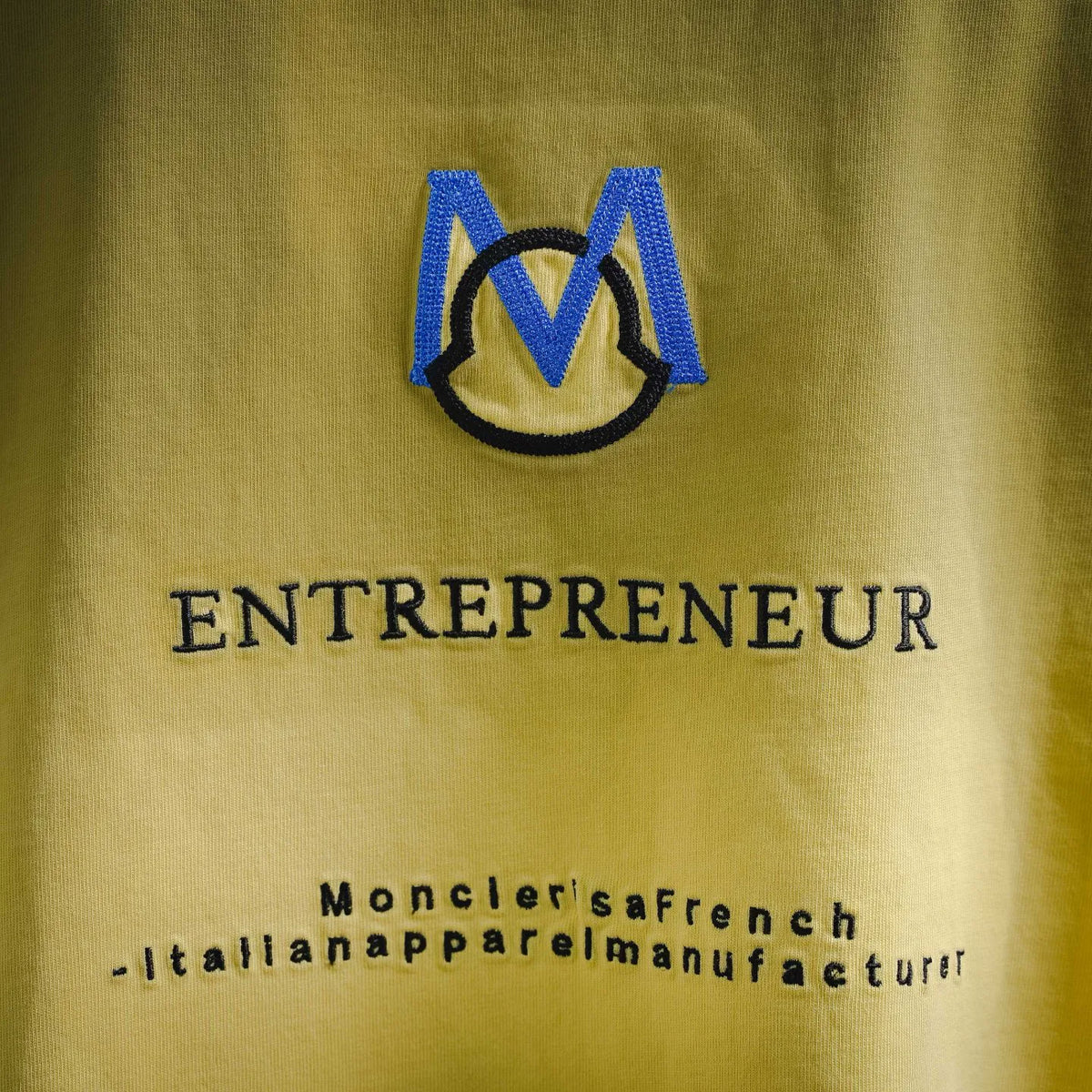 Men's yellow t-shirt back with blue M emblem and “ENTREPRENEUR” text