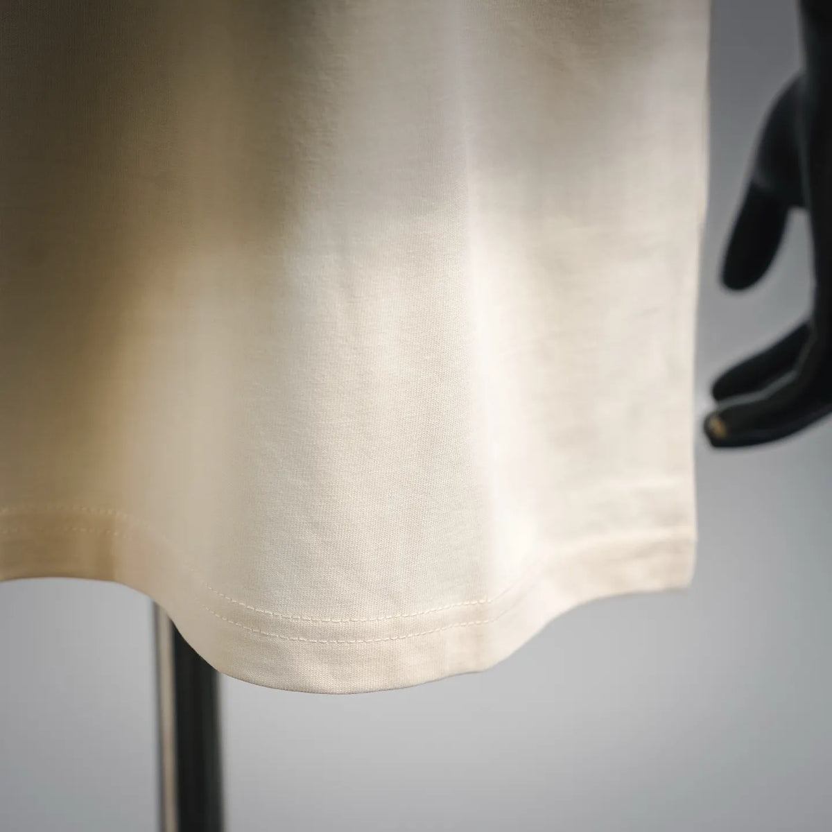 Cream T-shirt hem and side seam detail with short sleeves.