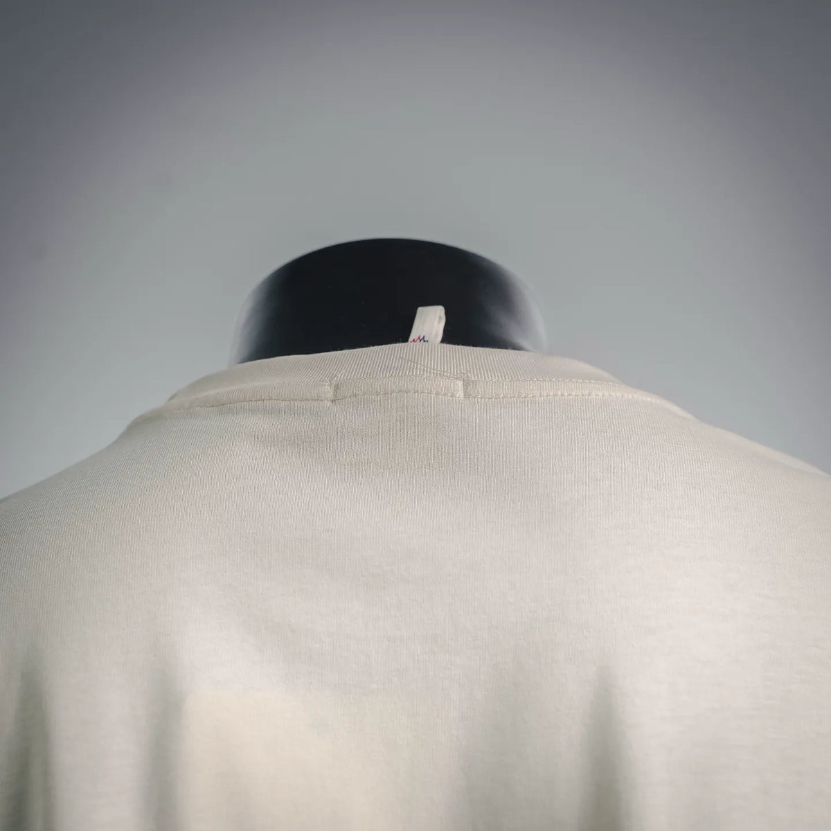 Cream T-shirt collar and upper back view with small logo tag area.