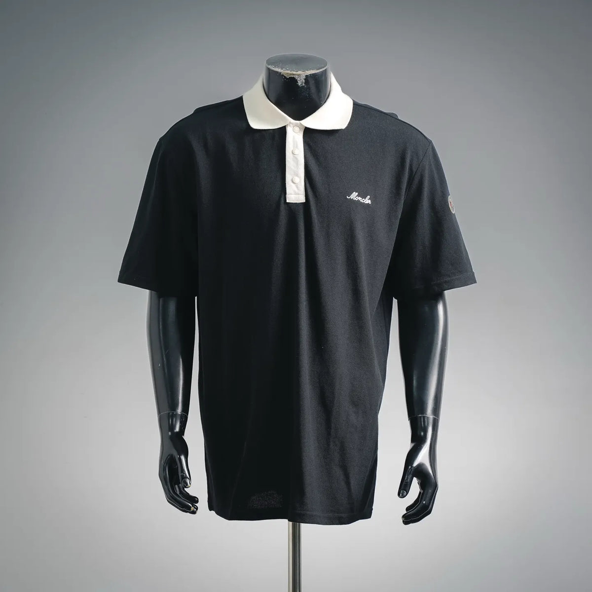 Black Moncler polo shirt with white collar and button placket on mannequin